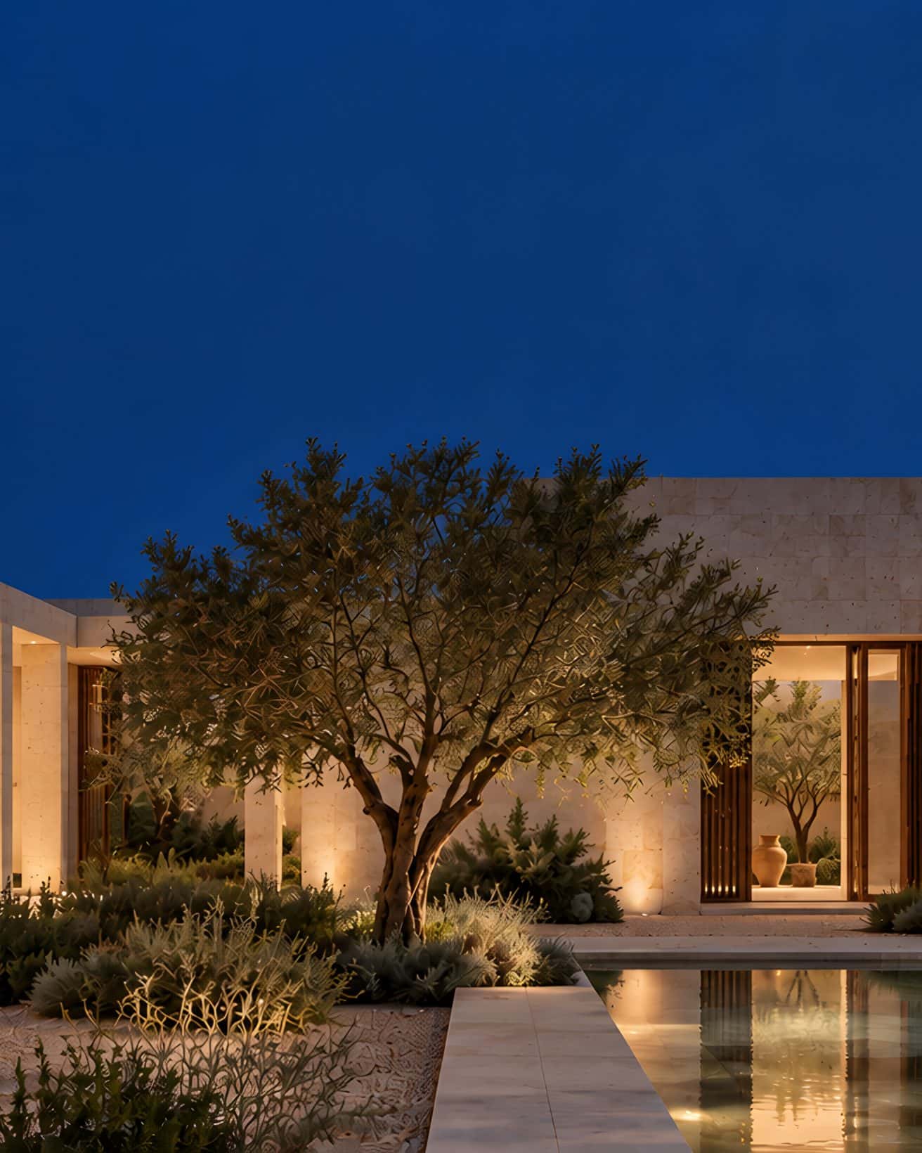 A limestone courtyard: a shaded colonnade, an olive tree, a stone bench and a still pool